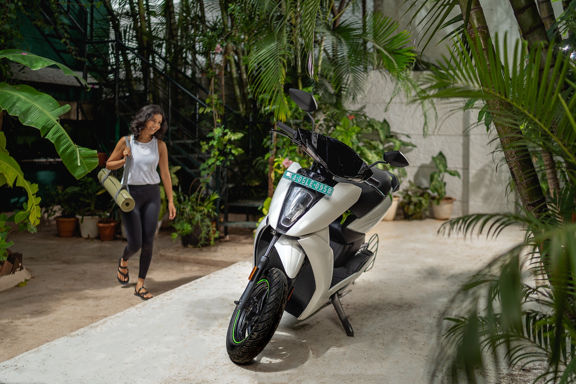 A photograph of a woman walking across a driveway towards an electric motorcycle.