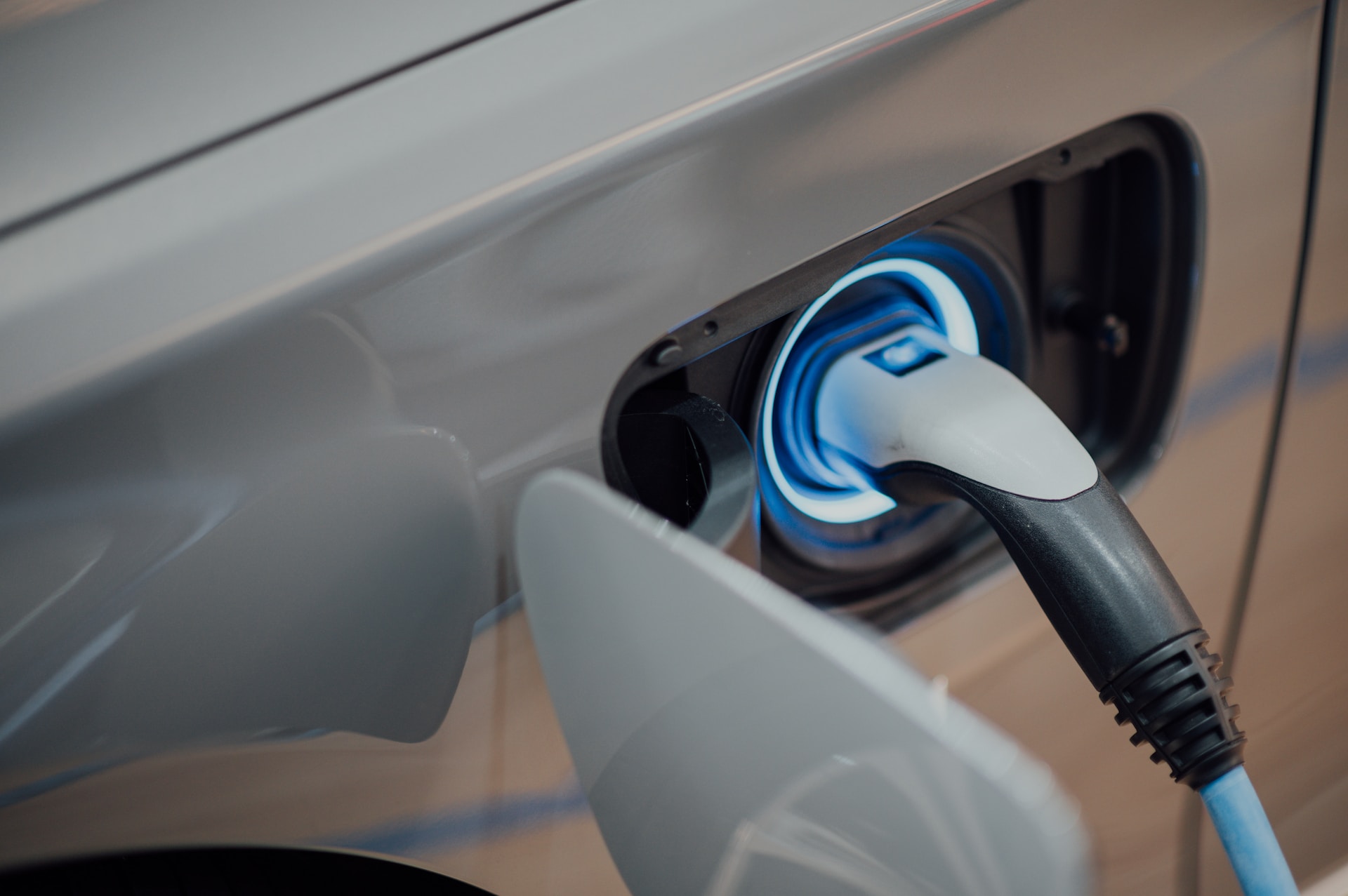 A photograph of a plugged-in electric vehicle charger, with a glowing blue LED light surrounding the charging plug. 