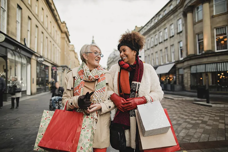 Image of two international doctors walking through a city centre holding shopping bags and laughing