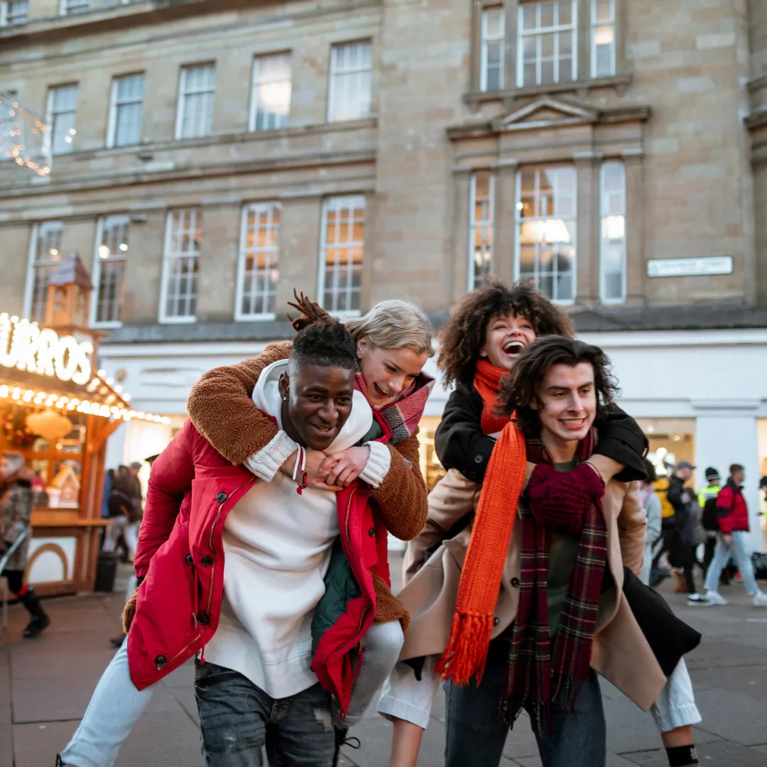 Image of 4 international doctors on each others shoulders, laughing outside a market.