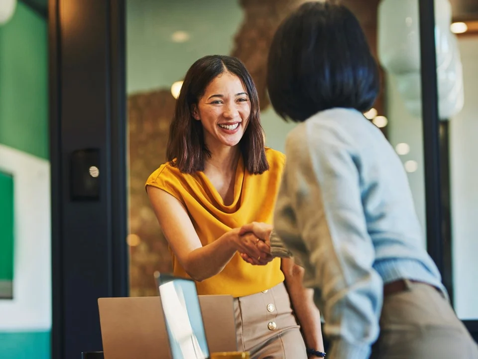 Business person in a yellow top shaking hands with a colleague