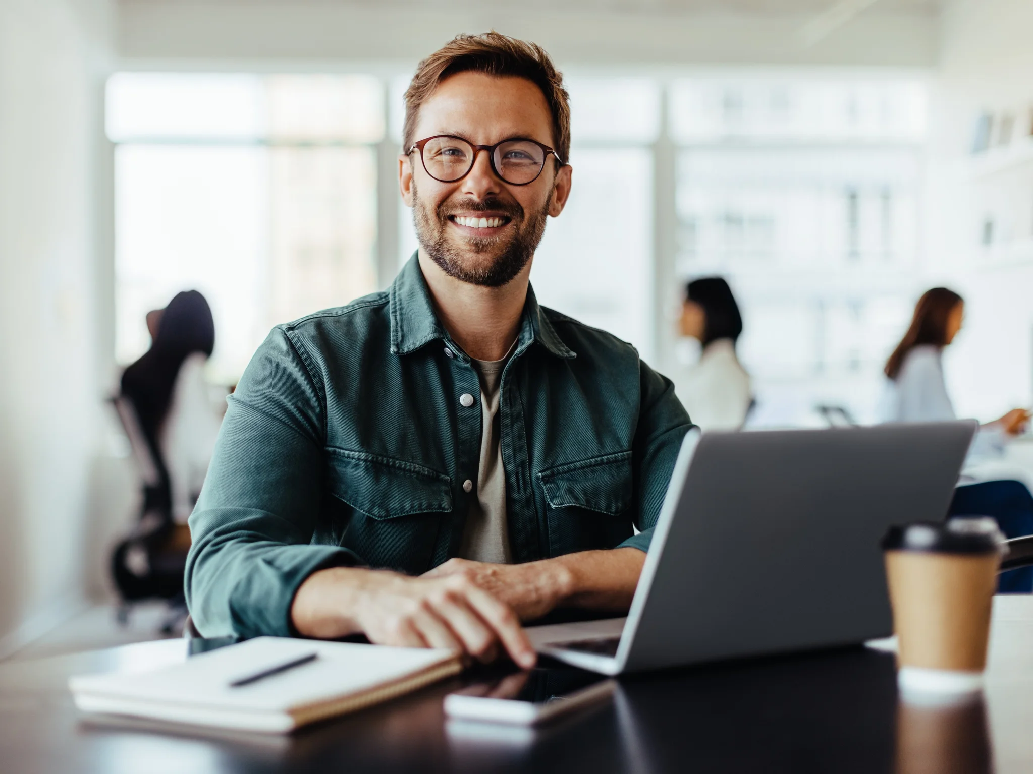 Smiling professional seated at a desk with a laptop in an office