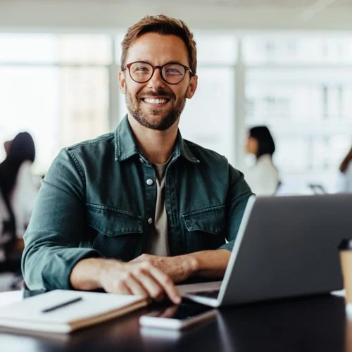 Business person sat at desk with laptop, notepad and phone