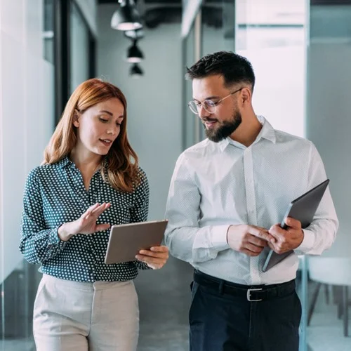 Business & Administration image Two business people walking through an office talking, whilst looking at a tablet