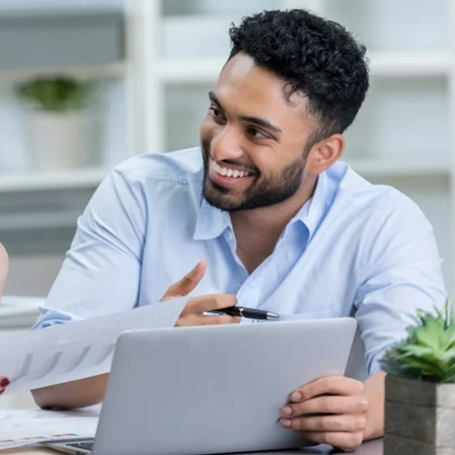 Businessperson sat at a laptop discussing work with colleague