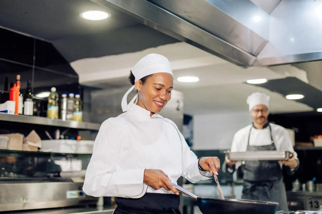 A smiling commis chef cooking in a kitchen