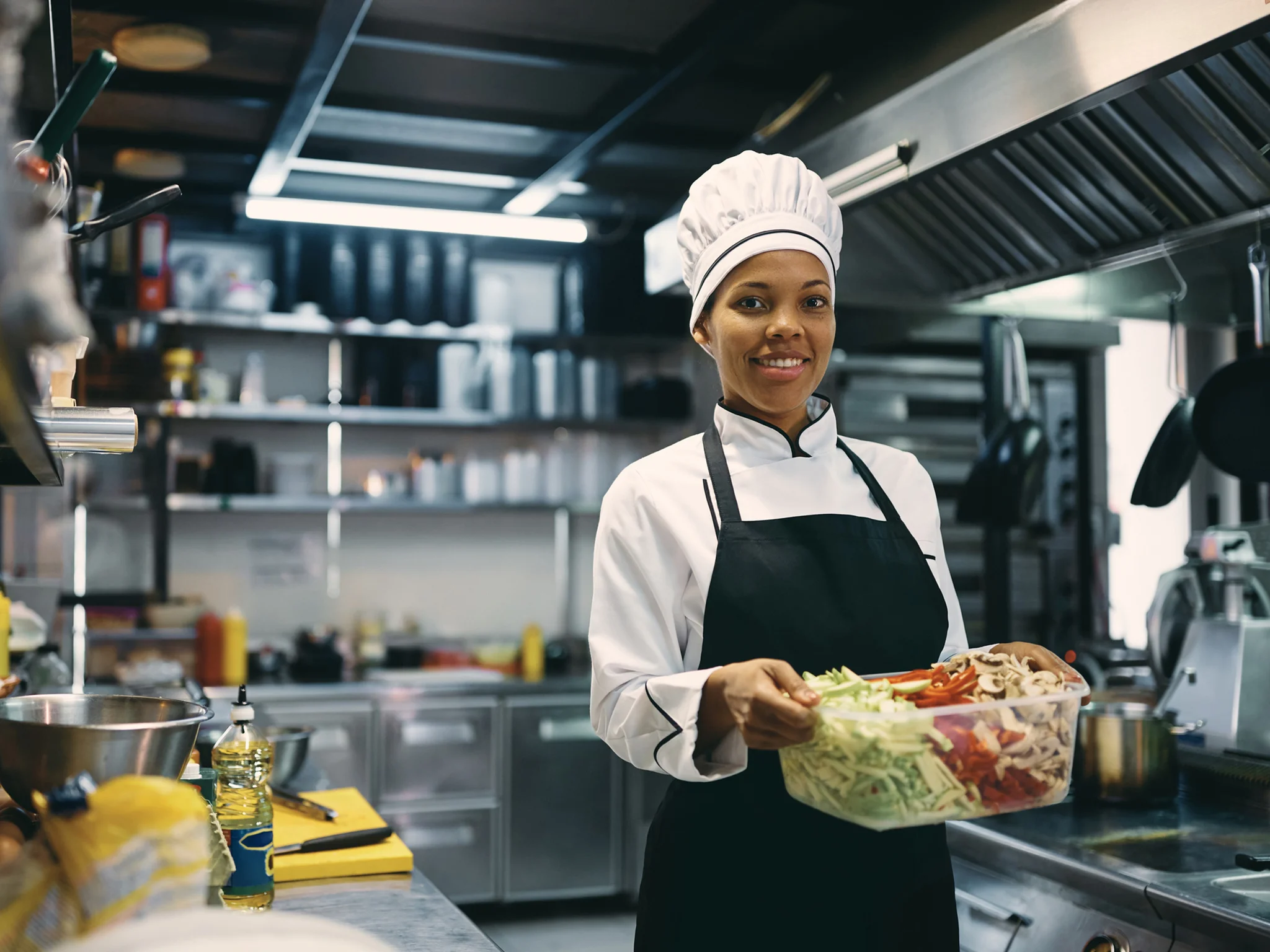Smiling Commis Chef holding a container full of chopped vegetables