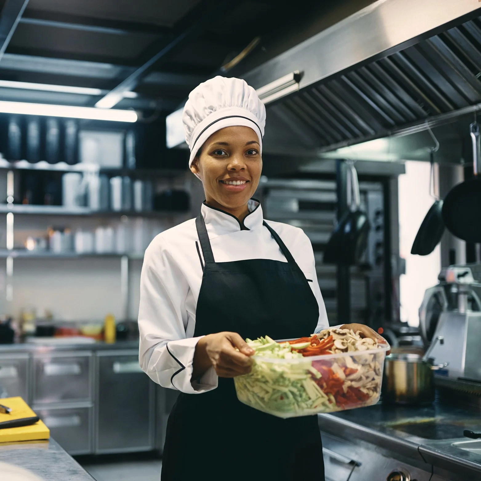 A smiling Commis Chef holding a container full of chopped vegetables
