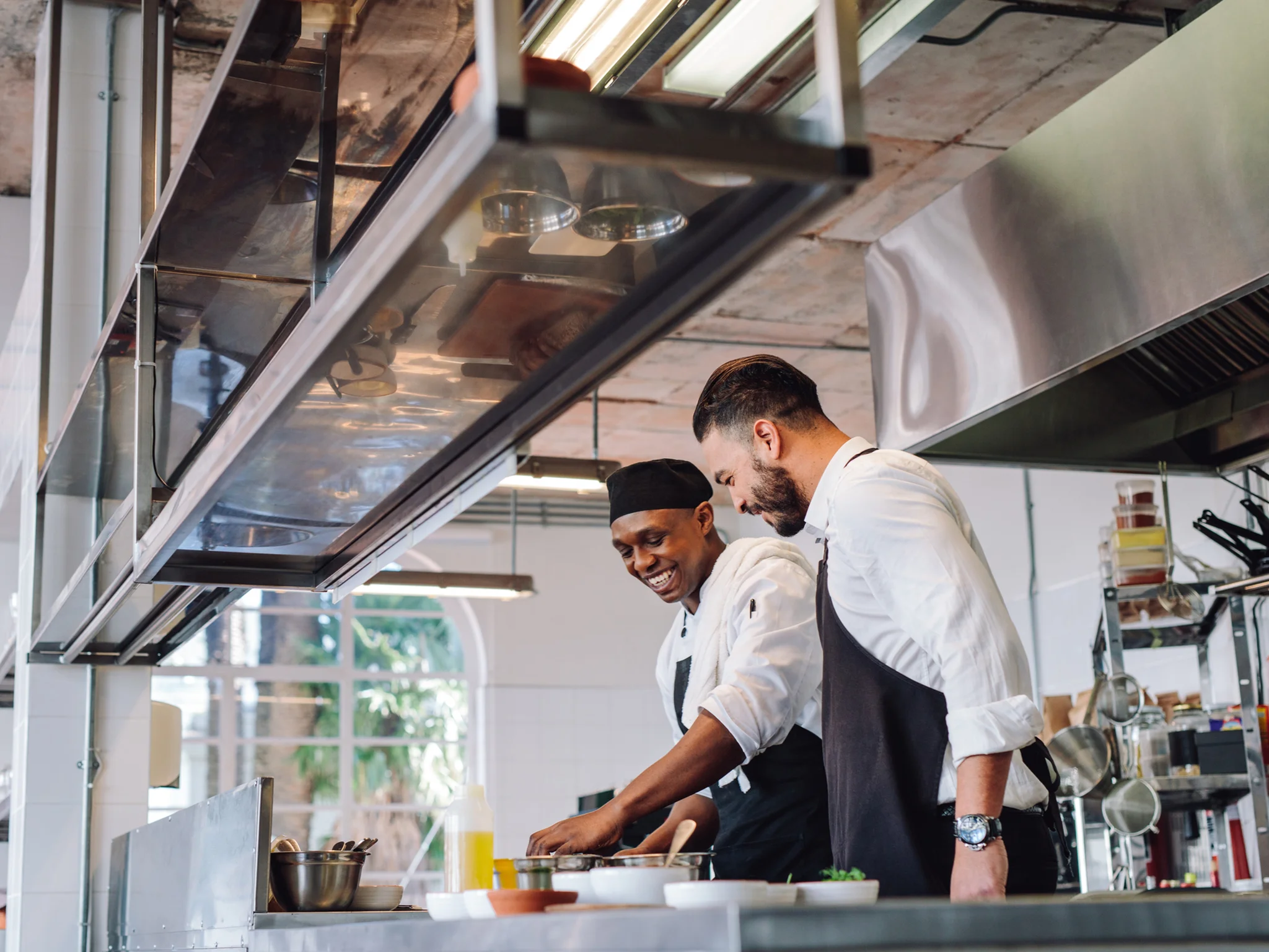 A smiling Commis Chef preparing food with a senior Chef