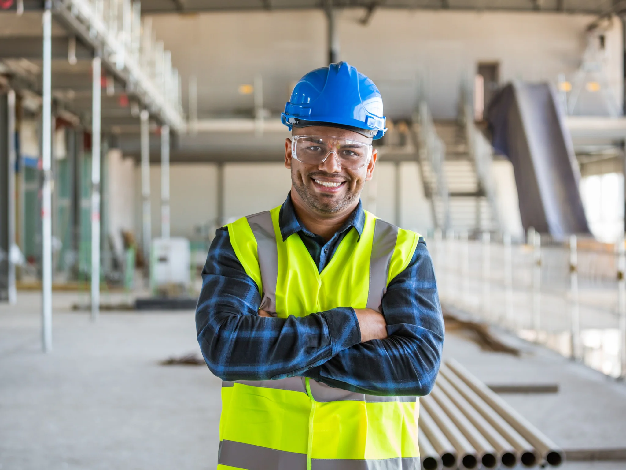 Smiling Electrical Engineer wearing a blue hard hat, safety goggles and hi-vis vest