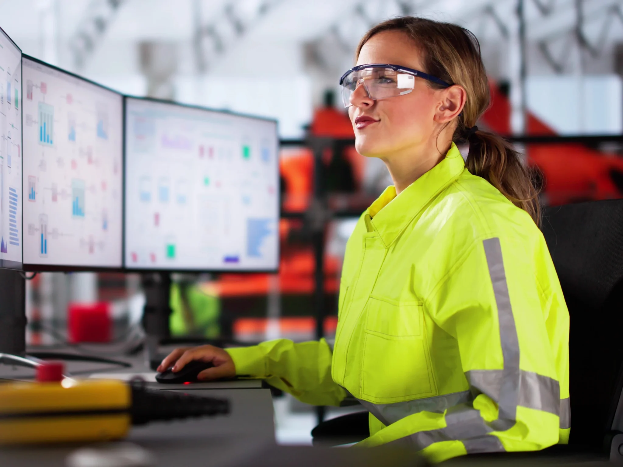 Engineer wearing a high-visibility yellow jacket monitoring screen in a control room