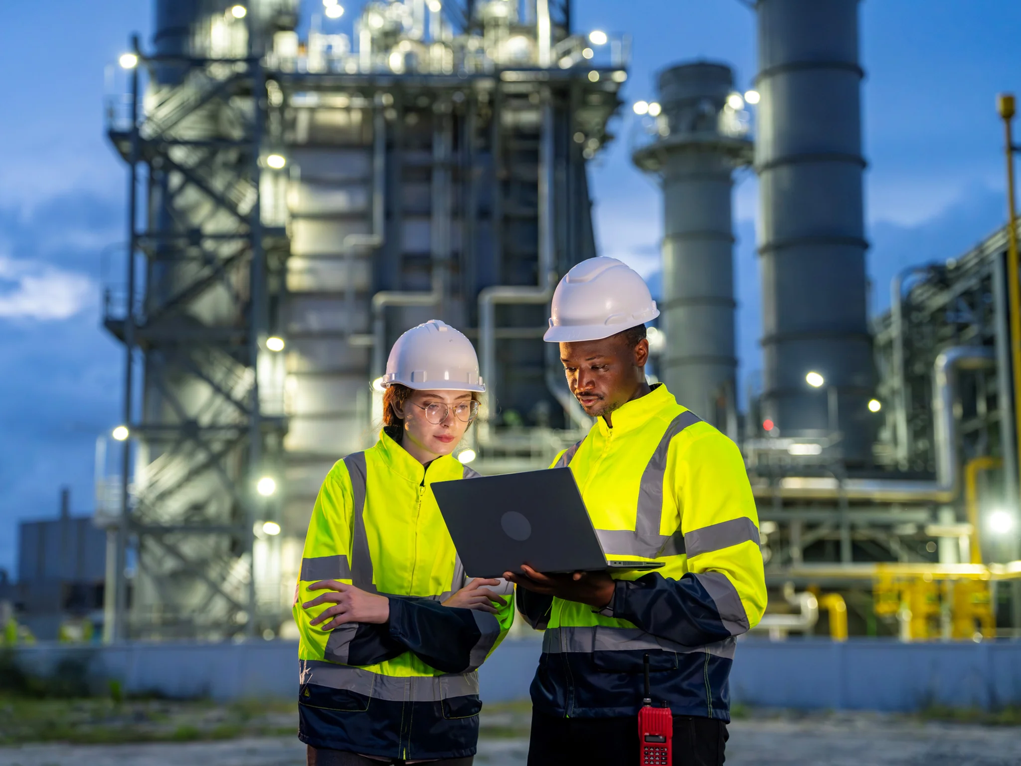 Two Engineers wearing high-visibility jacket and hard hats reviewing a laptop