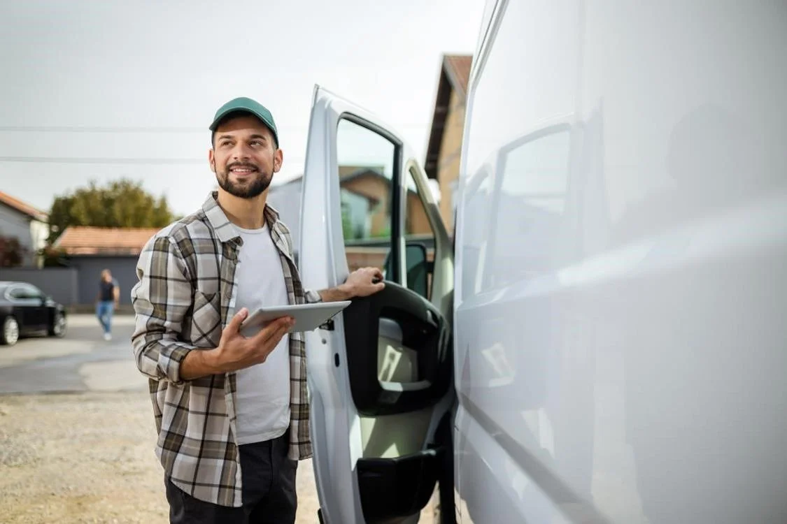 A drivers mate holding a tablet near a van 