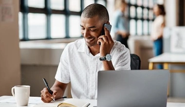 man smiling on phone at table with laptop