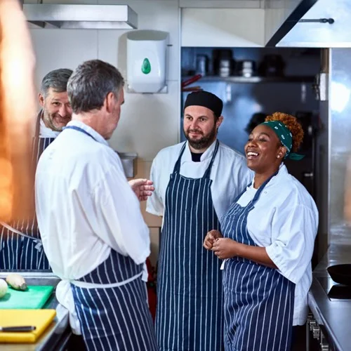 Hospitality & Catering image Four Kitchen staff wearing aprons stood talking in a kitchen