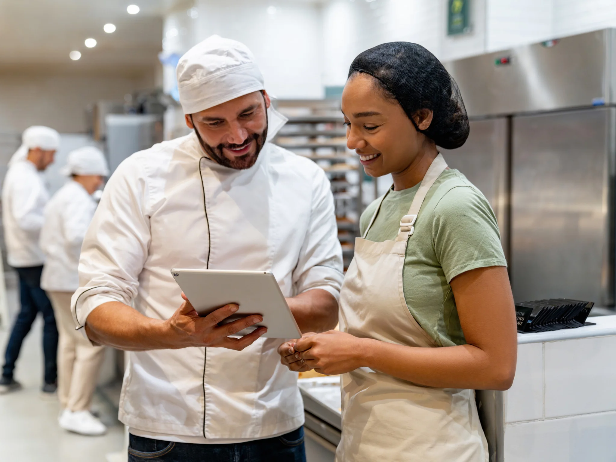 A Chef and Catering Assistant reviewing a tablet in a commercial kitchen