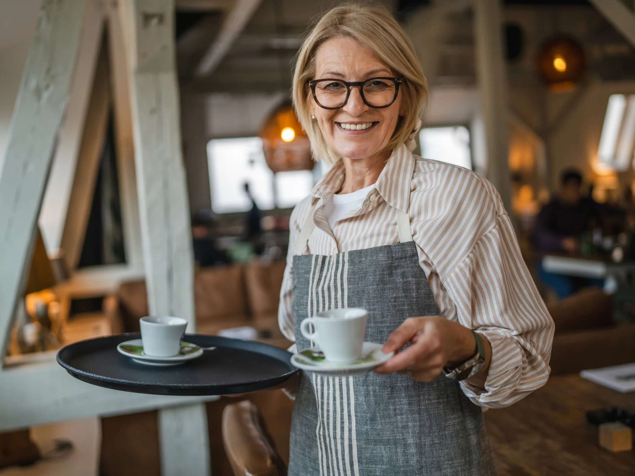 A smiling waitress wearing an apron serving coffee