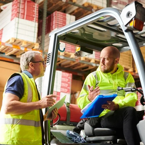 Reliable Talent Supply image Two warehouse workers wearing hi vis jackets. One sat in a forklift truck, the other stood holding a notebook.