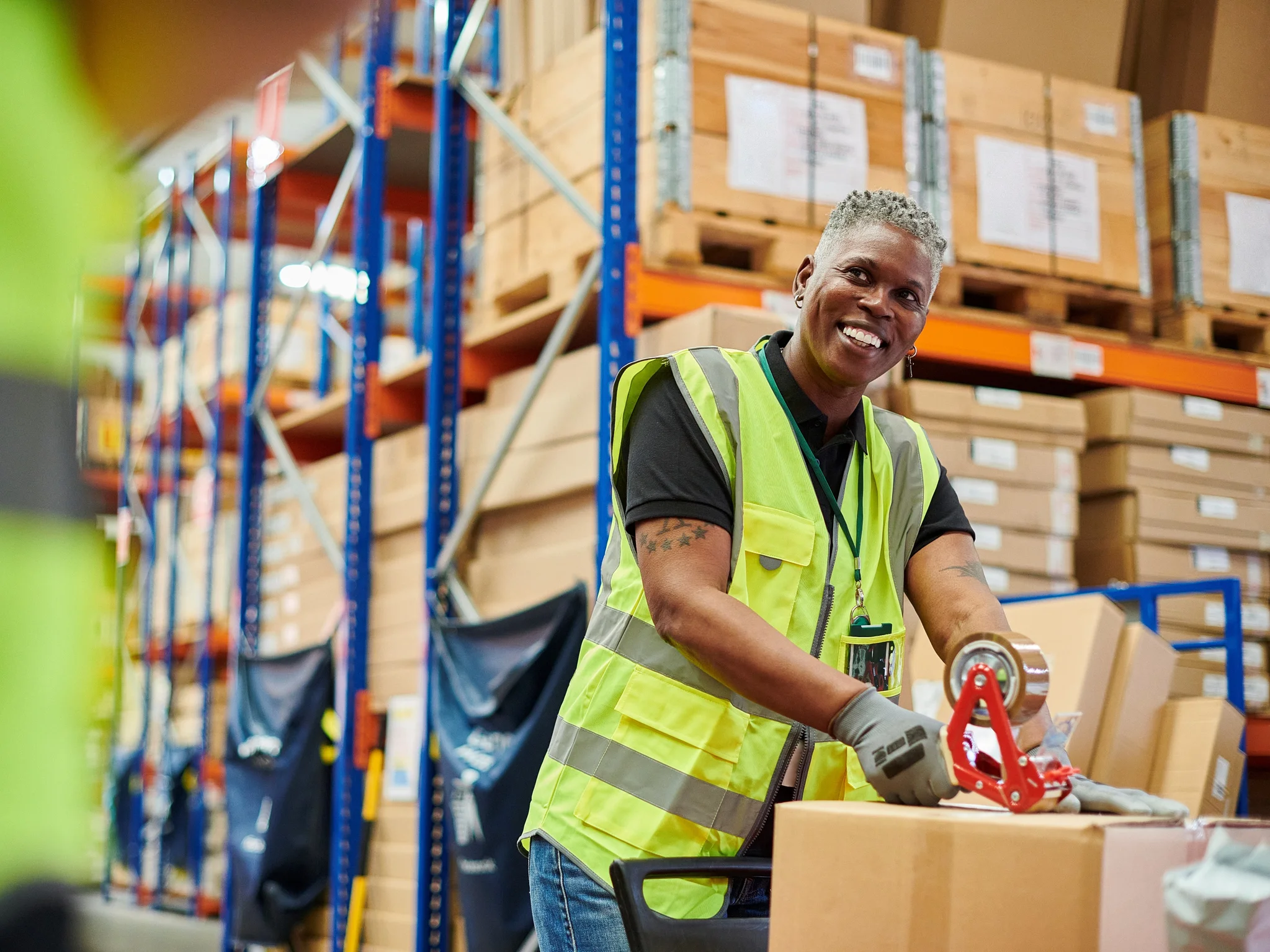 Warehouse worker smiling while sealing a parcel with tape