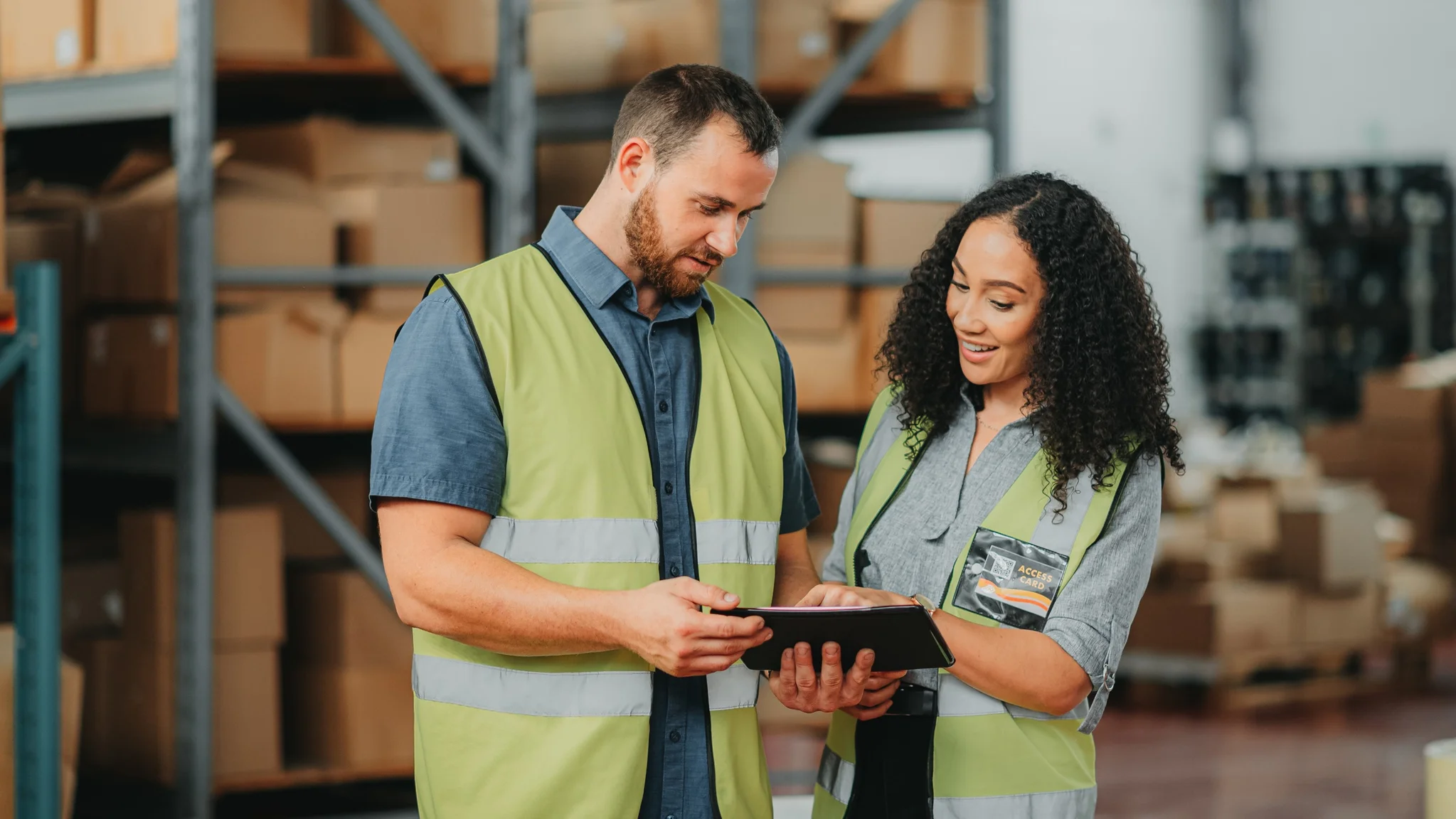 Two Warehouse Managers stood in a warehouse in yellow hi vis vests, looking at a tablet