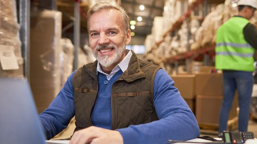 A Supply Chain Manager sat at a laptop in a busy warehouse