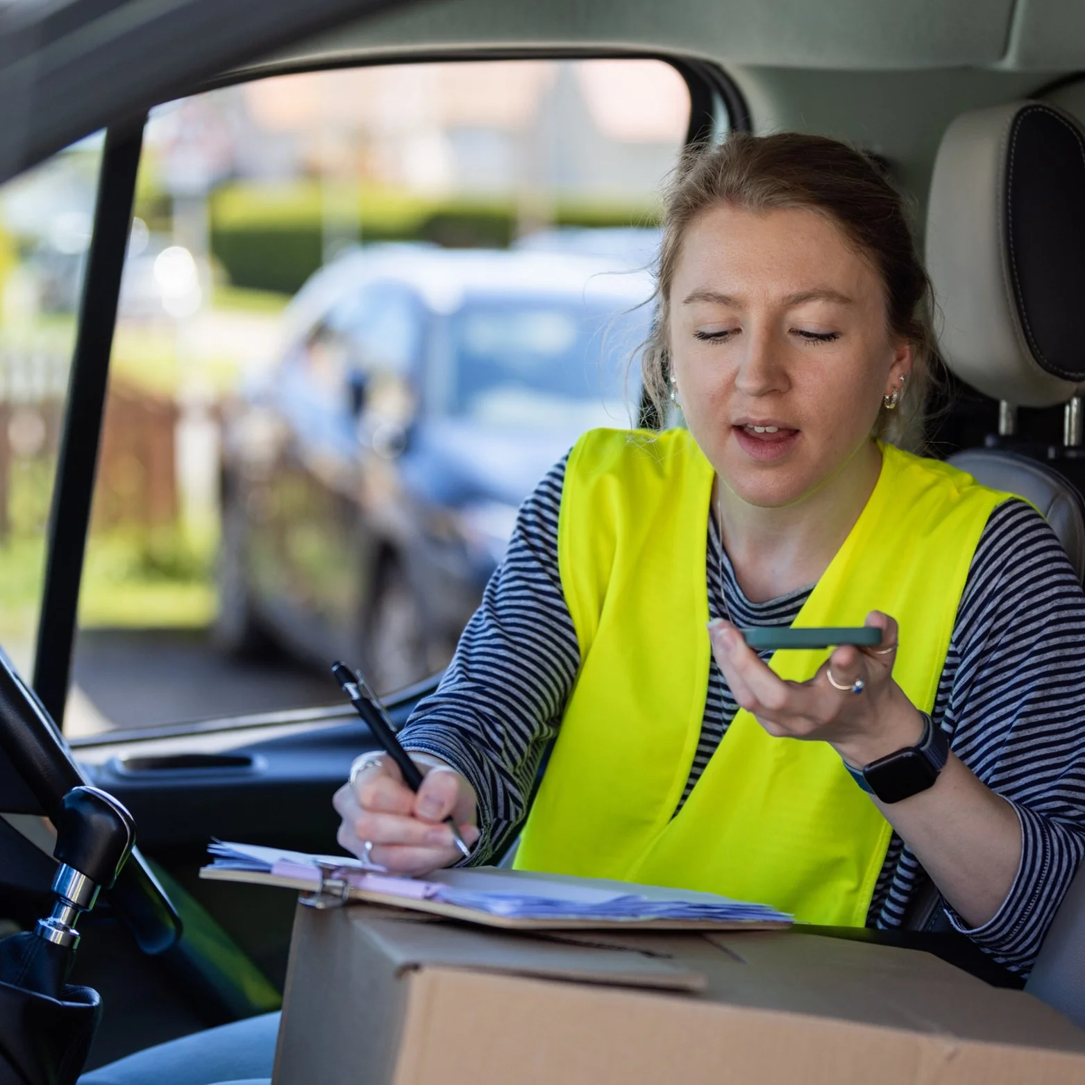 Delivery driver sitting inside a vehicle writing on a clipboard