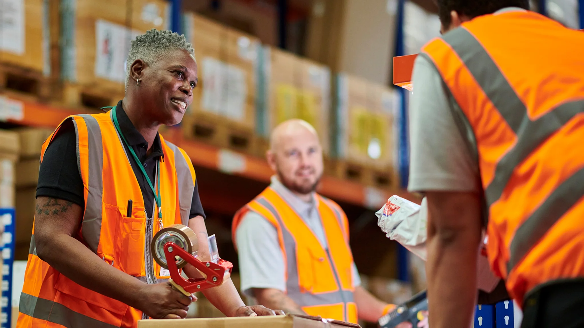 Warehouse worker in an orange hi vis vest taping up boxes
