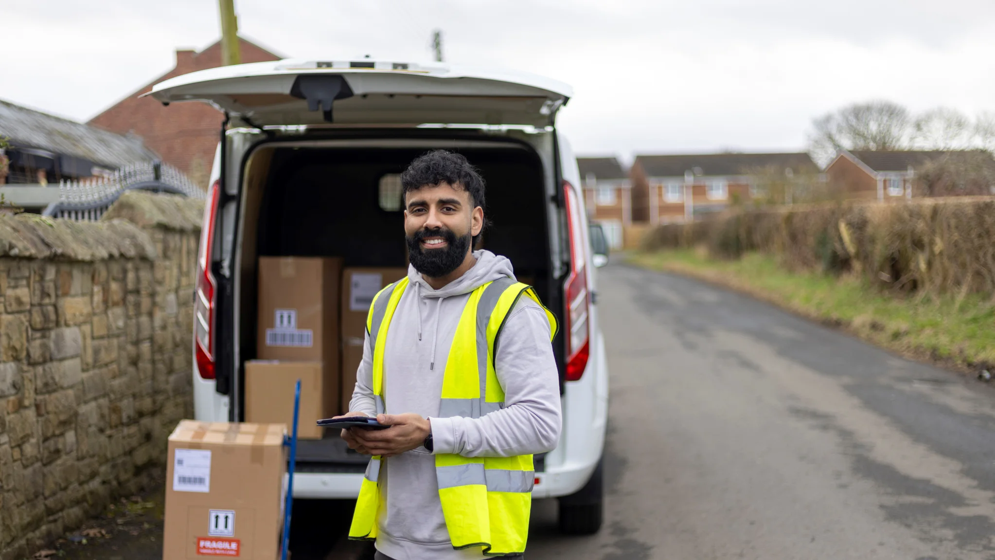Smiling delivery driver in front of an open white van loaded with parcels