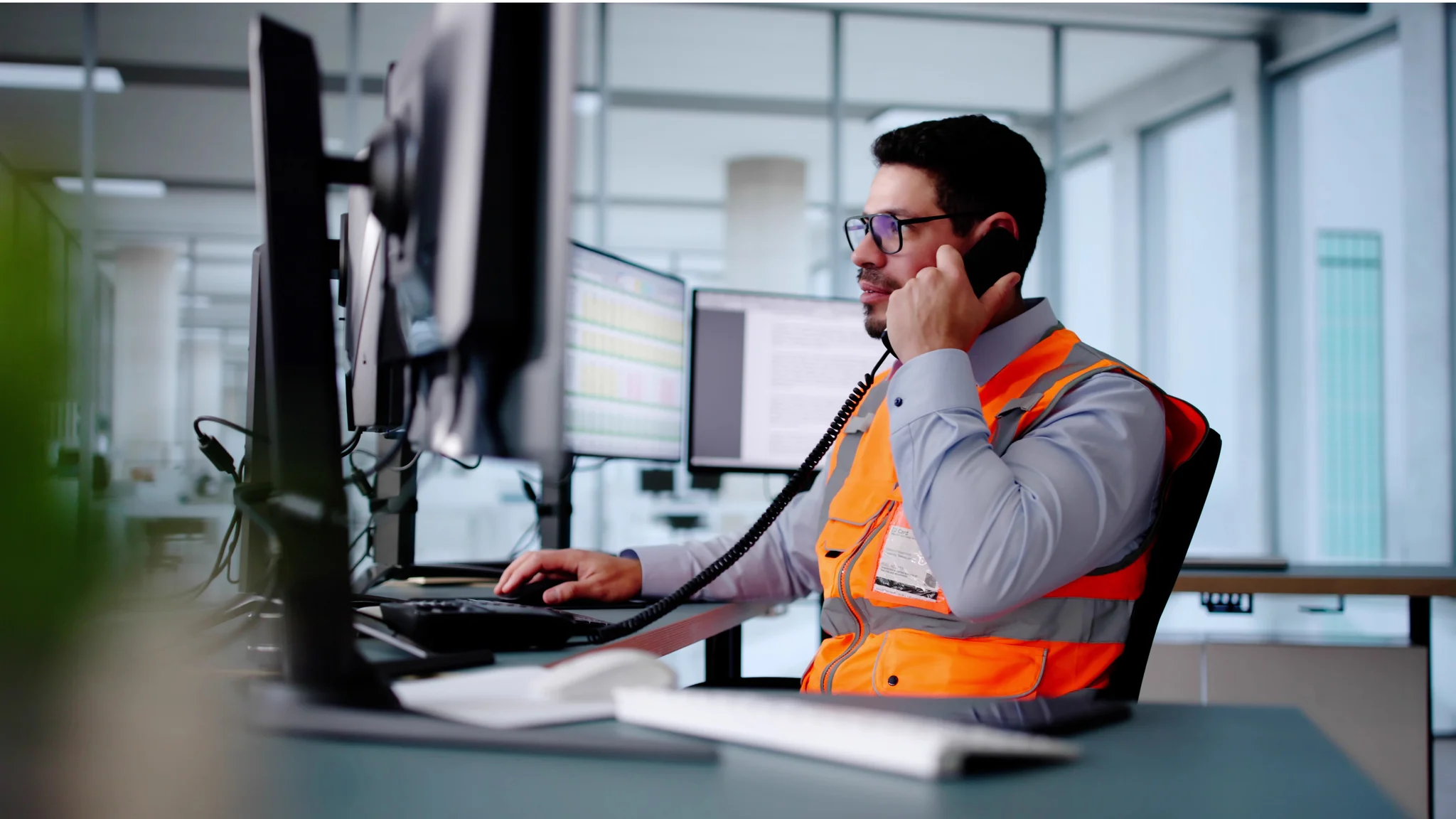 Logistics worker talking on a phone whilst using a computer with multiple monitors