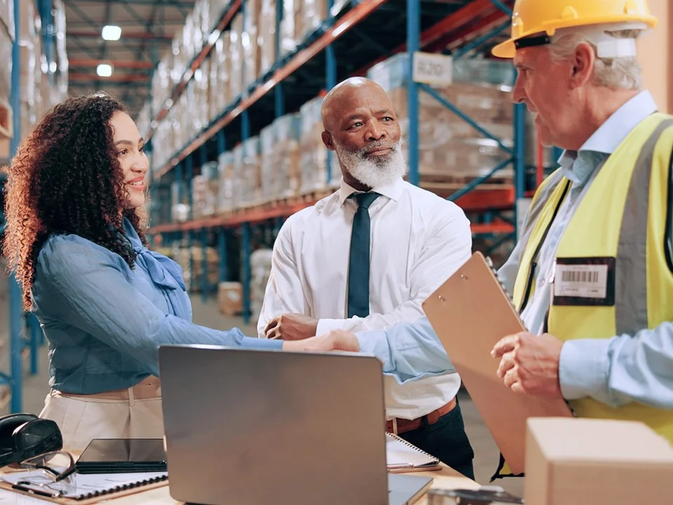 Three logistics leaders stood in front of a laptop in a warehouse
