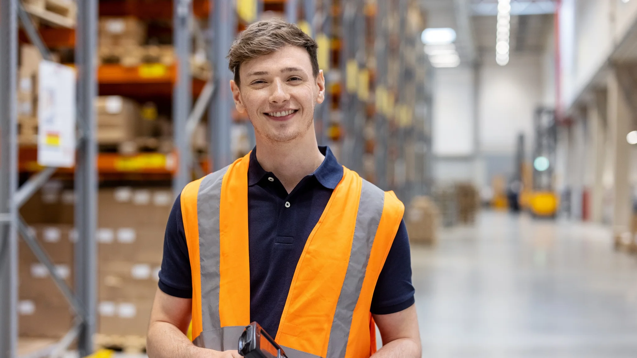 Warehouse operative stood in a warehouse wearing an orange hi vis vest