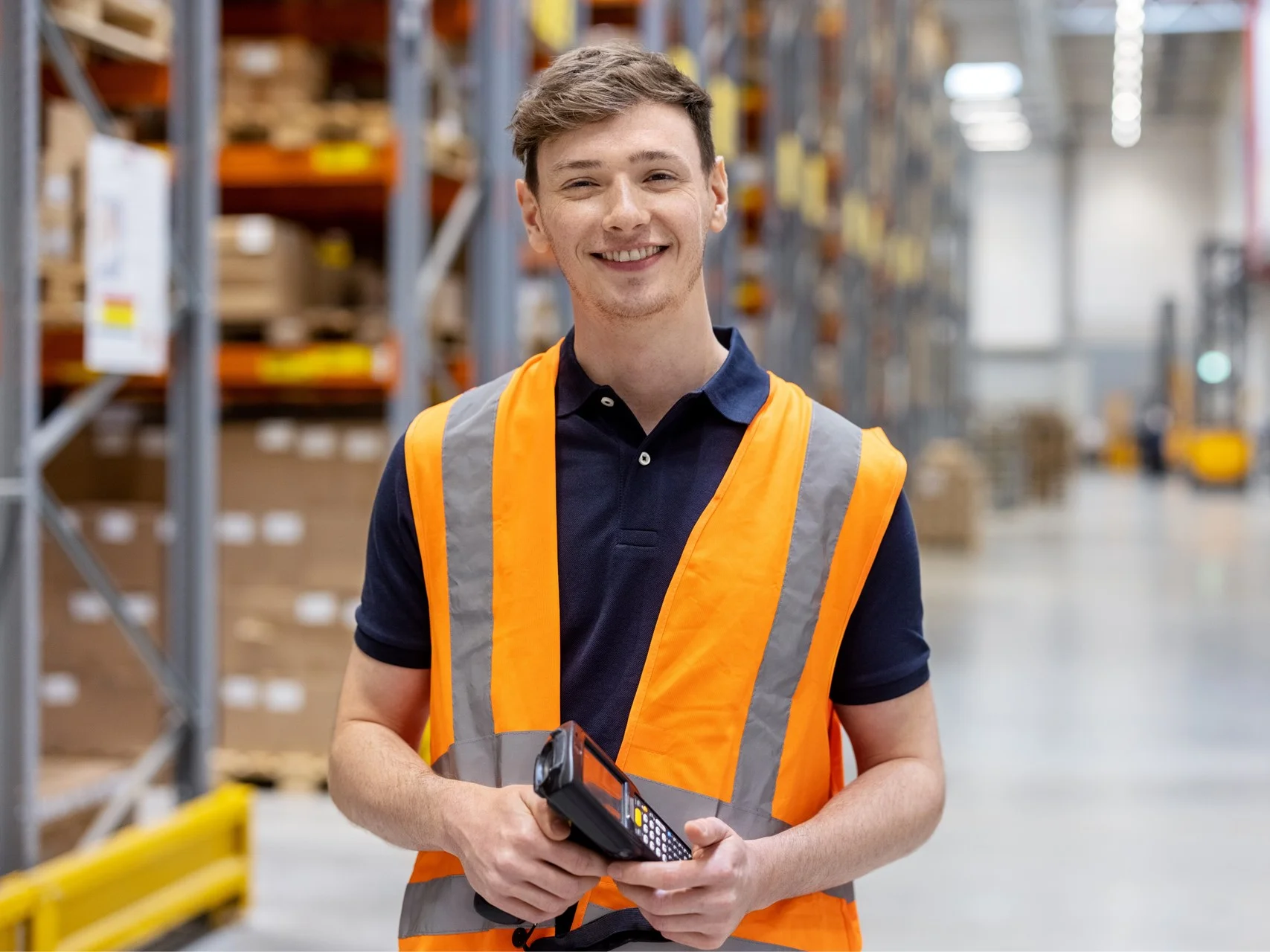 Smiling Warehouse Operative holding a scanner wearing an orange high-visibility vest