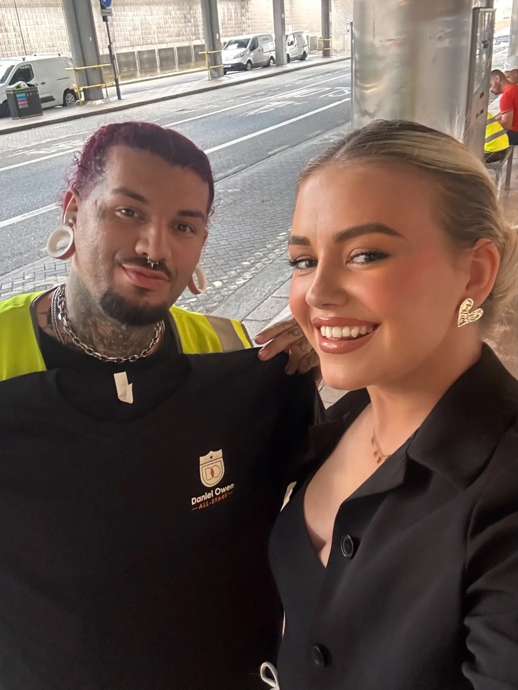 A female recruitment consultant and a male construction site worker. The recruitment consultant is smiling in frame whilst the construction worker is holding up a t-shirt gifted to him by the consultant for his hard work on construction sites.