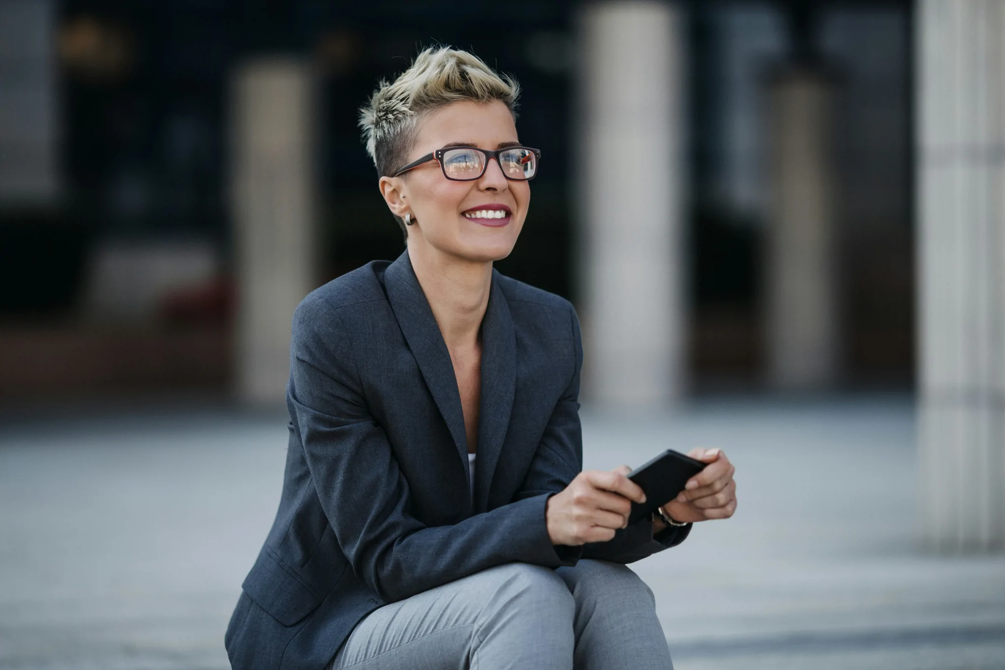 lady wearing glasses dressed smart sitting down outside looking into distance