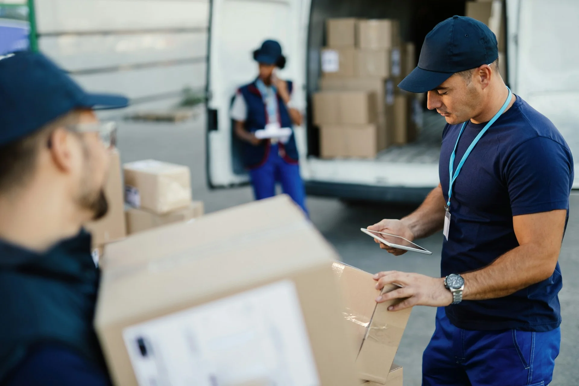 young-delivery-man-using-touchpad-and-checking-packages-while-organizing-a-delivery-with-his-coworkers-