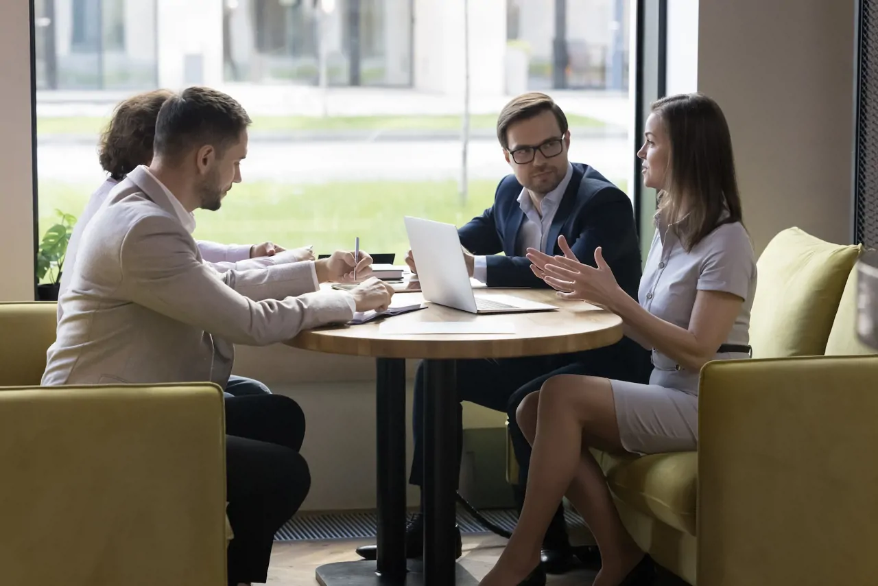 A group of people sitting on green chairs at a table having a meeting