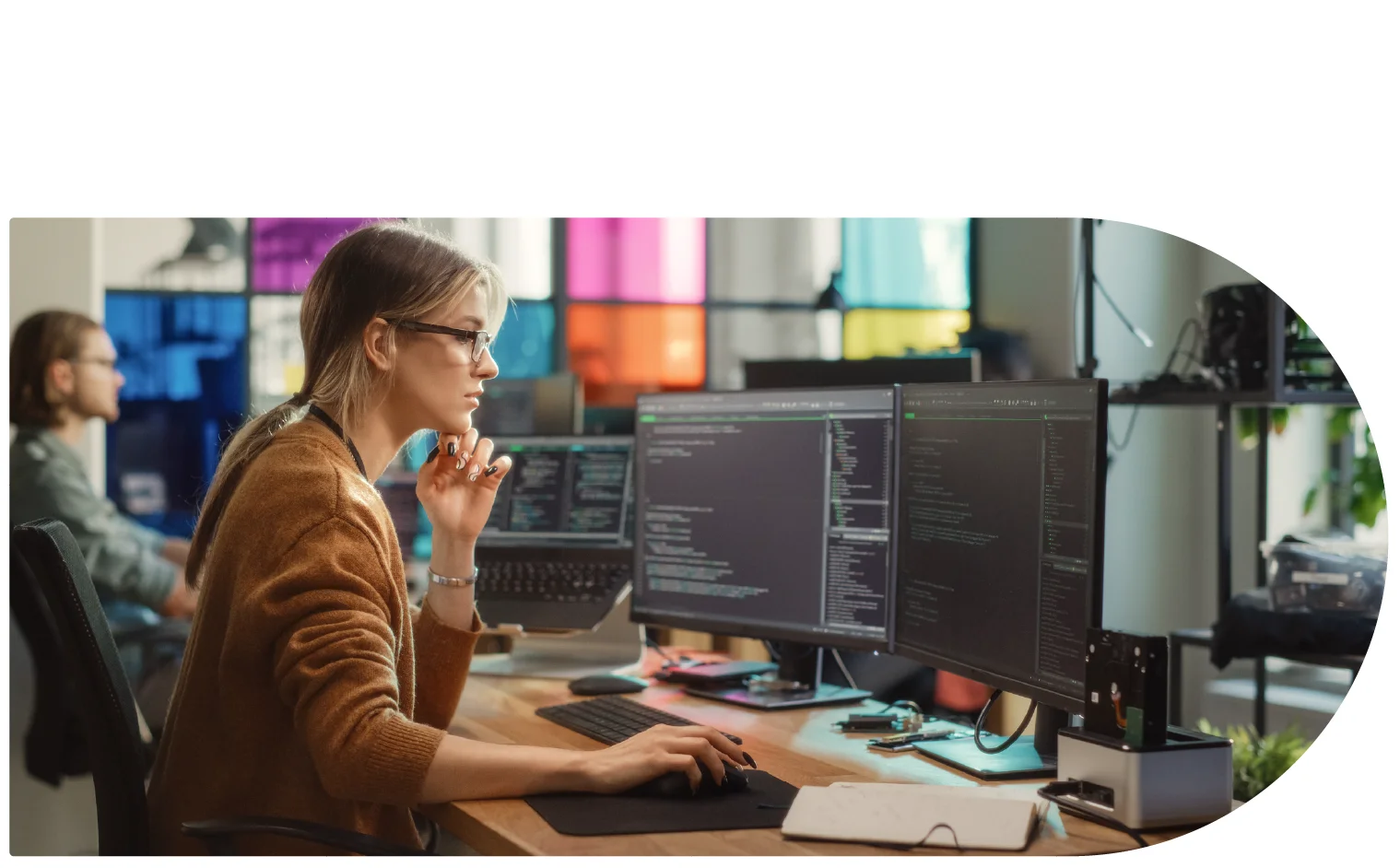A woman sat a desk looking at a computer with multiple screens.