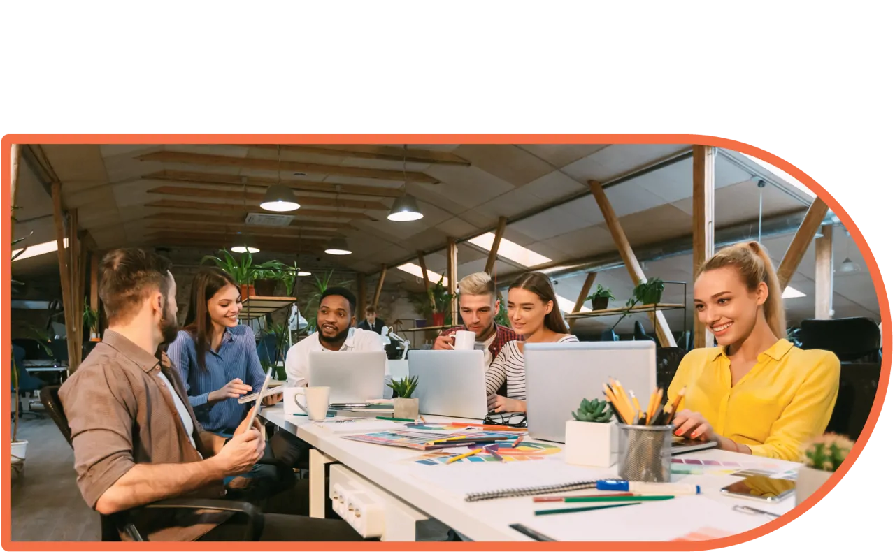 A team of relaxed and happy people sat around a table, looking at laptops