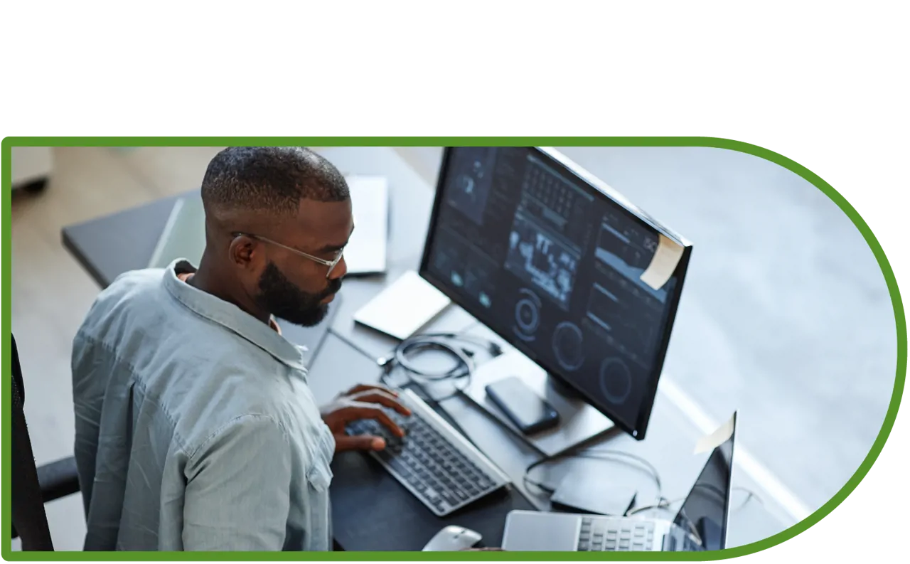 A man sat a desk looking at a computer with multiple screens.