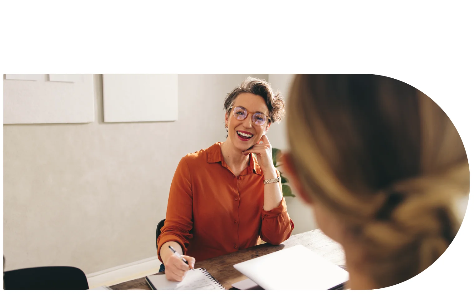 A woman at a conference table laughing with another person in the foreground.