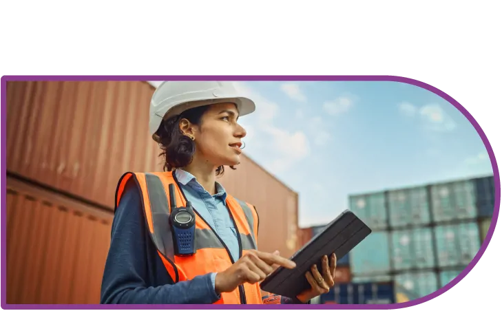 A woman in a hard hat and a high vis vest outside. She is holding a tablet and has a walkie talkie on her jacket.