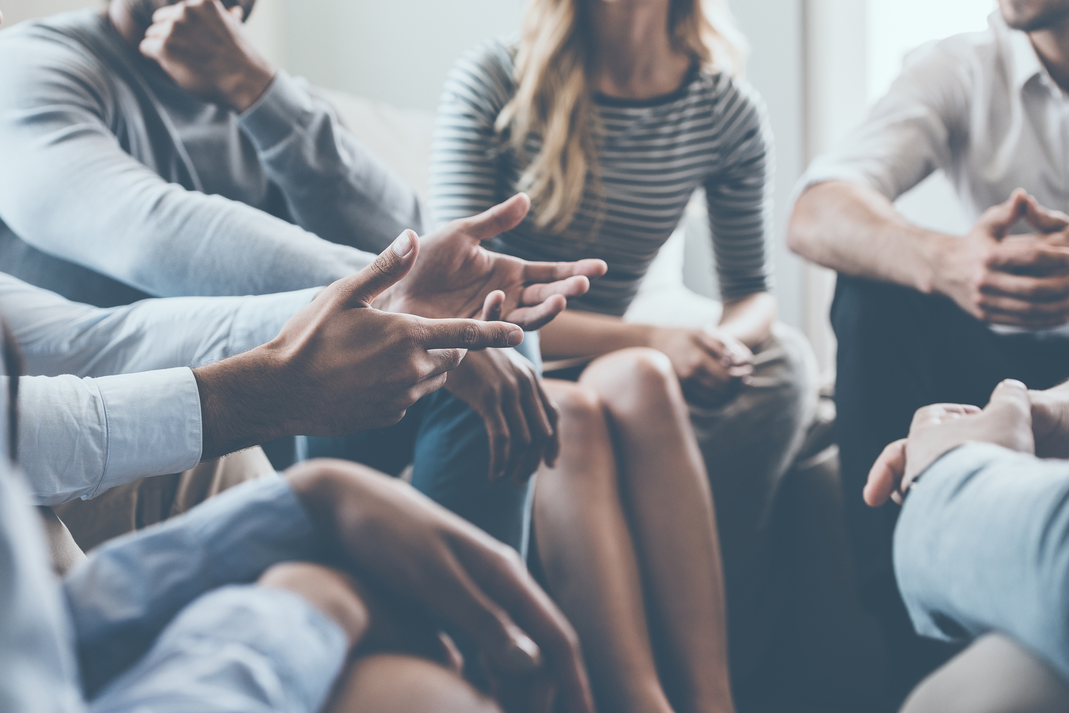 A photo of a group of people sitting in a circle. You can only see their hands, and one person is gesturing with their hands as if talking animatedly. 