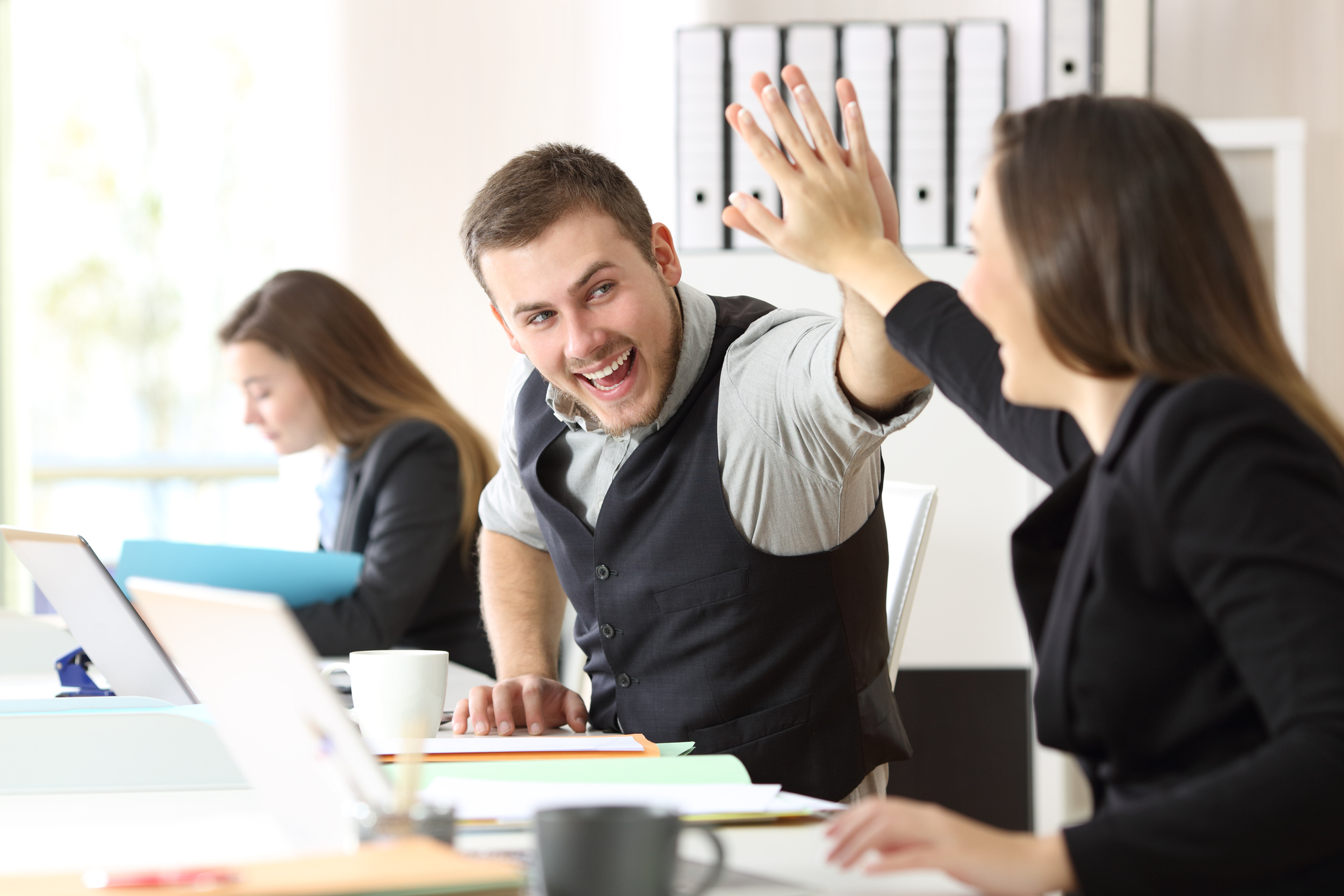 A photo of a woman and a man in an office environment. They are high-fiving eachother, and the man is smiling.