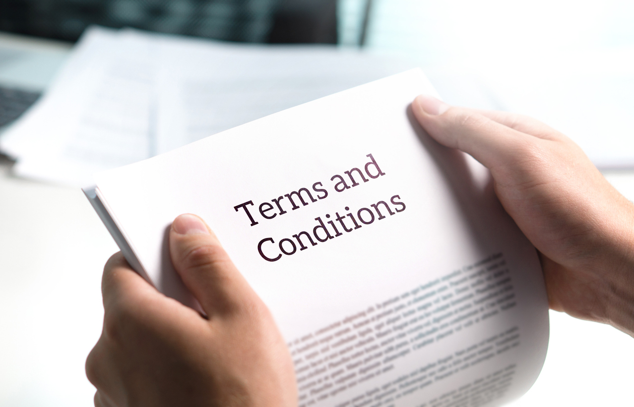 A person holding a document with terms and conditions printed on it. You can only see the person's hands holding the document.