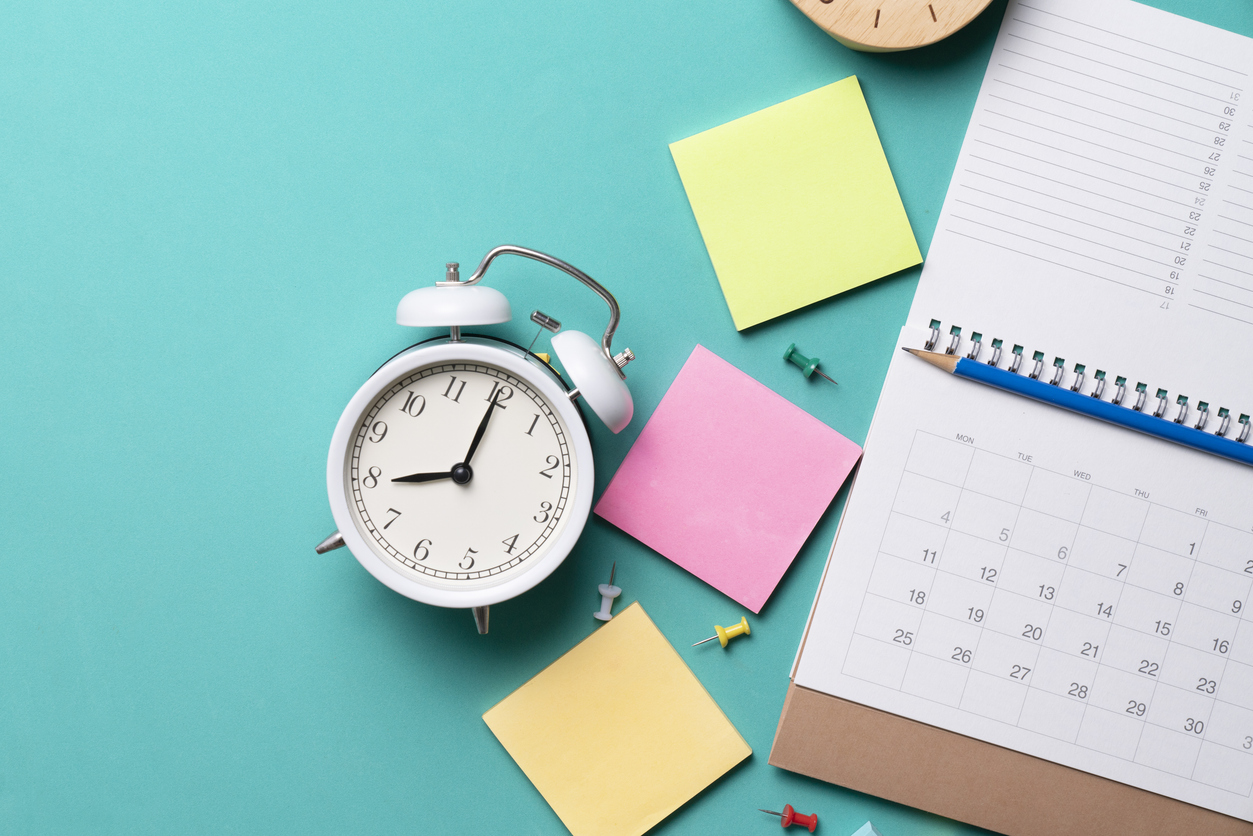 A image of an alarm clock, a calendar, and an array of stationery laid out on a flat surface. The image could symbolise organisation and productivity.