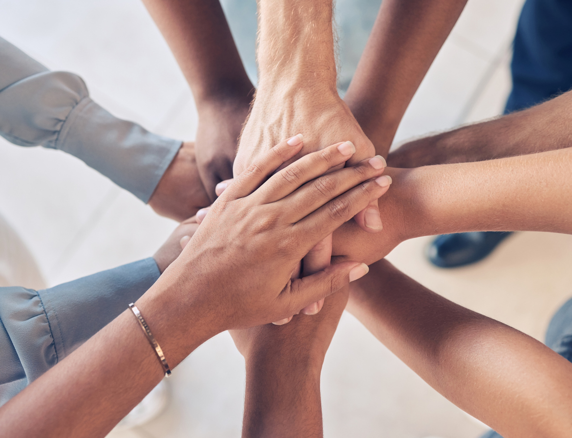 An image of eight hands on top of each other to symbolise unity and team work. The hands are the hands of people from different diversities. 