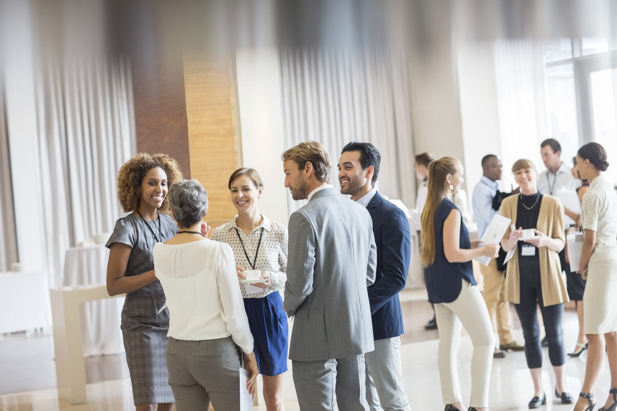 A photo of a group of people at a networking event. They are dressed in smart clothing and talking to each other smiling.