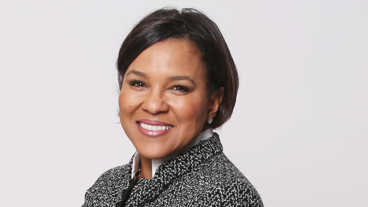 A portrait of business woman and trailblazer Rosalind Brewer. She is a successful CEO, and is known for calling out a lack of diversity in business. She has brown skin, dark brown hair and is smiling at the camera.