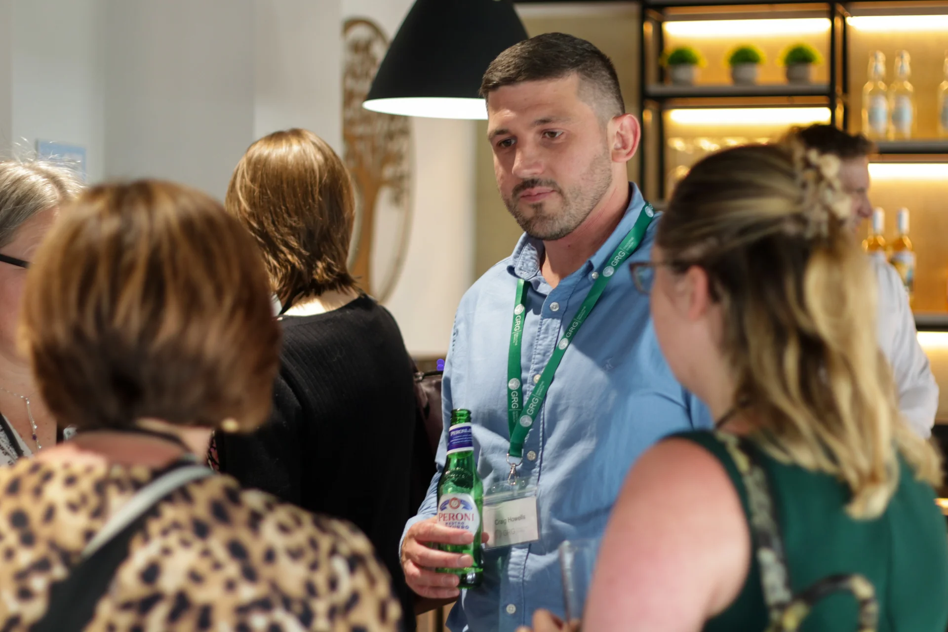 A photo of a GRG Executive Search consultant networking at a company event. He is tall with dark hair and can be seen chatting to a group of female senior professionals.