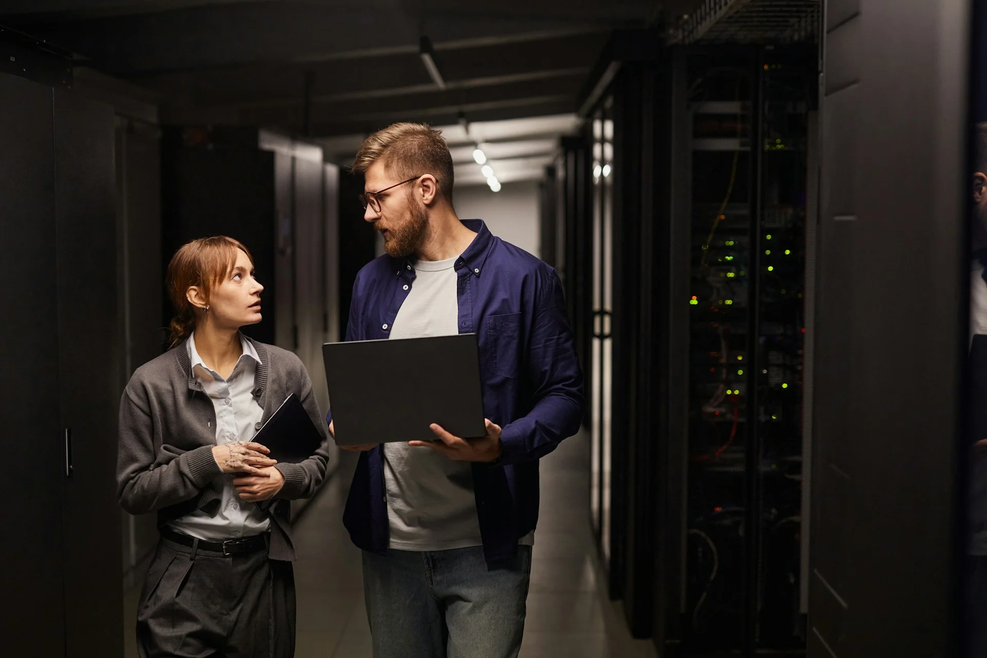 two-it-professionals-discussing-tasks-while-holding-equipment-in-data-center-server-room-surrounded-by-servers-and-technology-